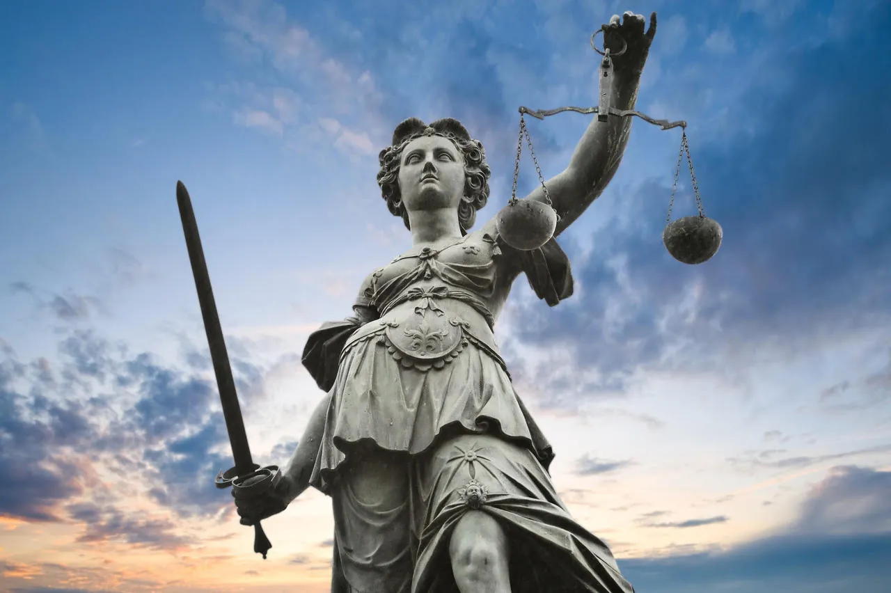 Escultura de la Justicia con balanza y espada bajo un cielo luminoso